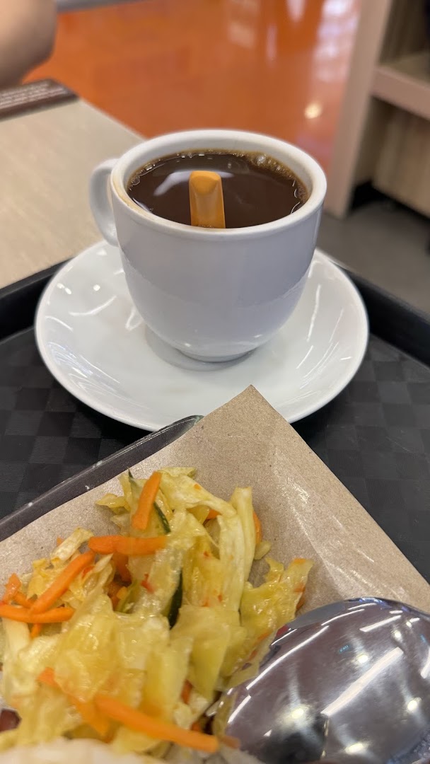 A close-up of a hot coffee with a biscuit stick, served alongside a side dish of pickled vegetables.