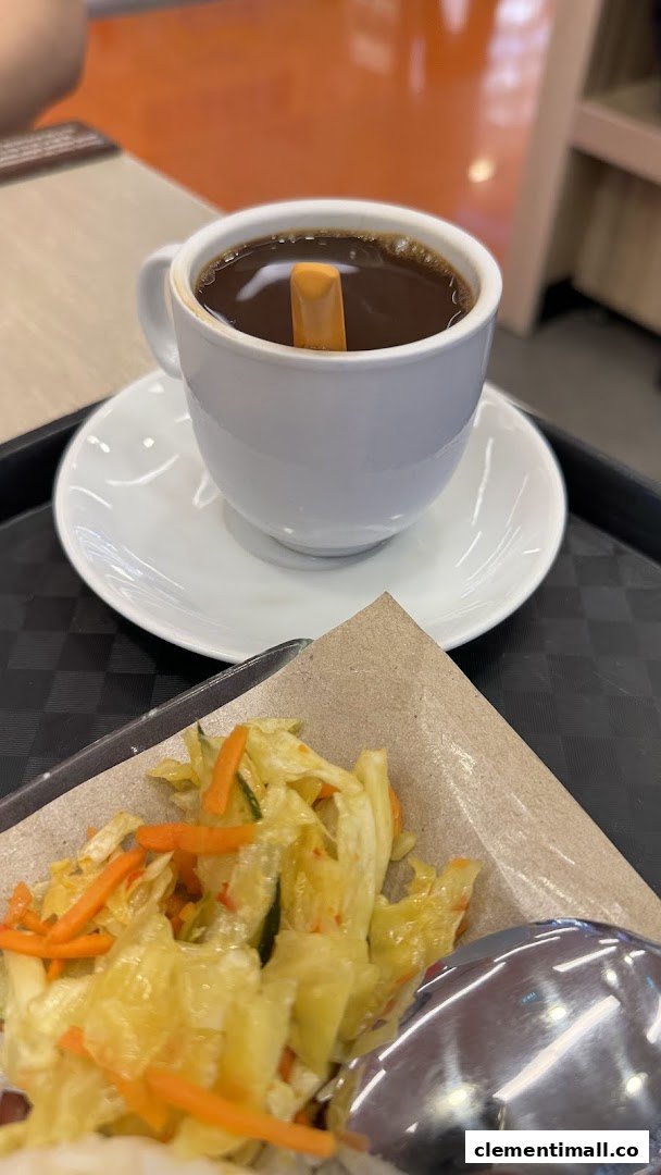 A close-up of a hot coffee with a biscuit stick, served alongside a side dish of pickled vegetables.