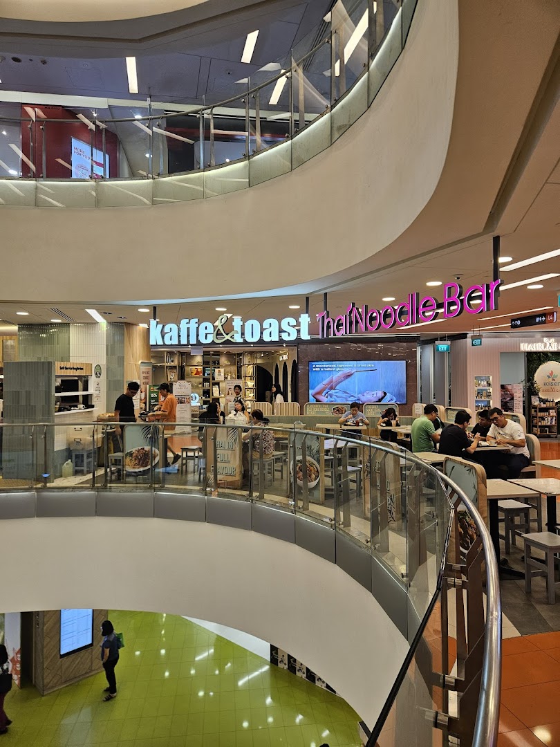 Diners enjoy meals at Kaffe & Toast Thai Noodle Bar within a bustling shopping mall environment.