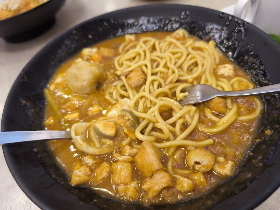 A close-up of a delicious noodle dish with a rich sauce, meatballs, and other ingredients in a black bowl.