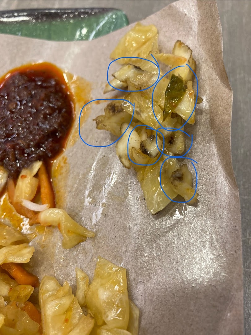 Close-up of a side dish featuring pickled vegetables and a rich sauce, served on paper.