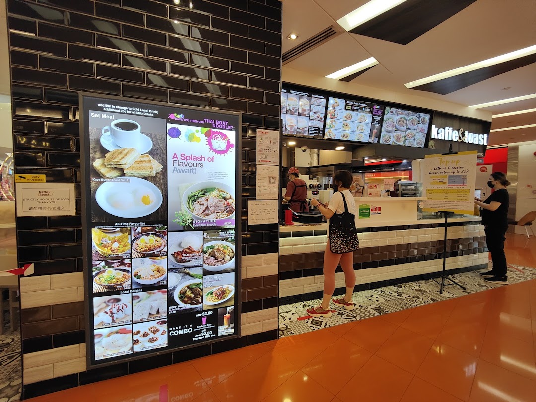 A food stall counter with digital menu boards displaying various Thai and local dishes, with customers ordering.