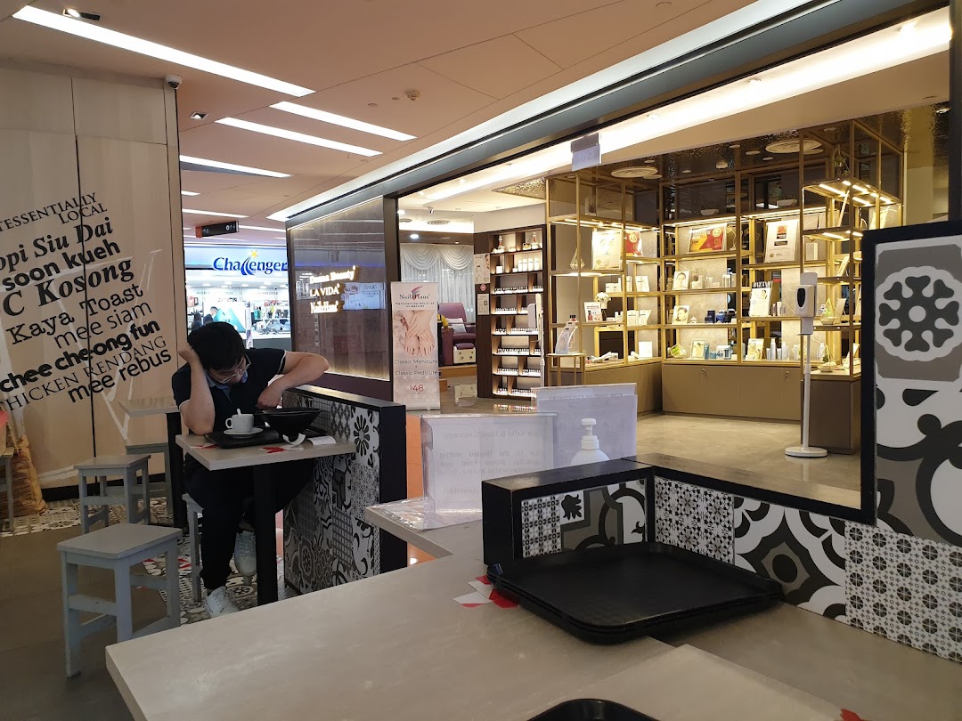 An interior shot of Kaffe Toast Thai Noodle Bar, showing a customer dining and adjacent mall shops.