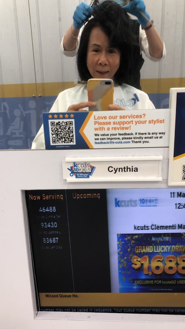 A customer receives a haircut at kcuts, with a queue management screen and feedback sign visible.