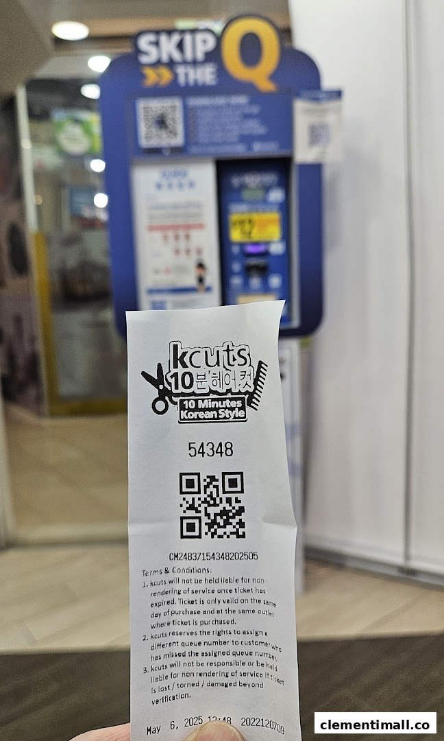 A customer holds a kcuts queue ticket in front of the 'SKIP THE Q' self-service machine.