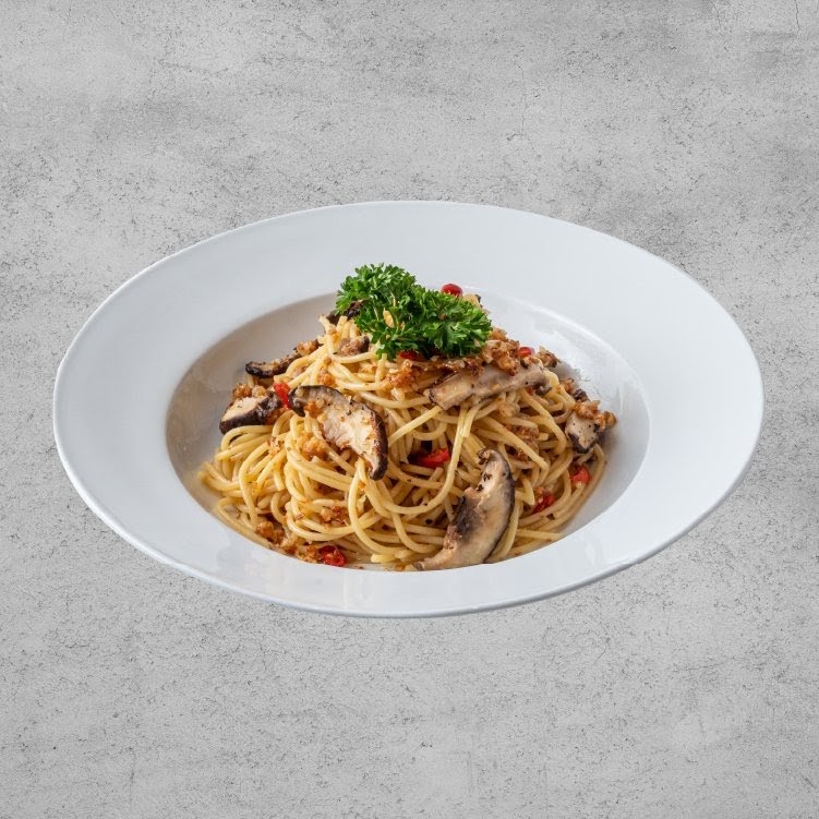A delicious plate of spaghetti with mushrooms, chili, and herbs in a white bowl.
