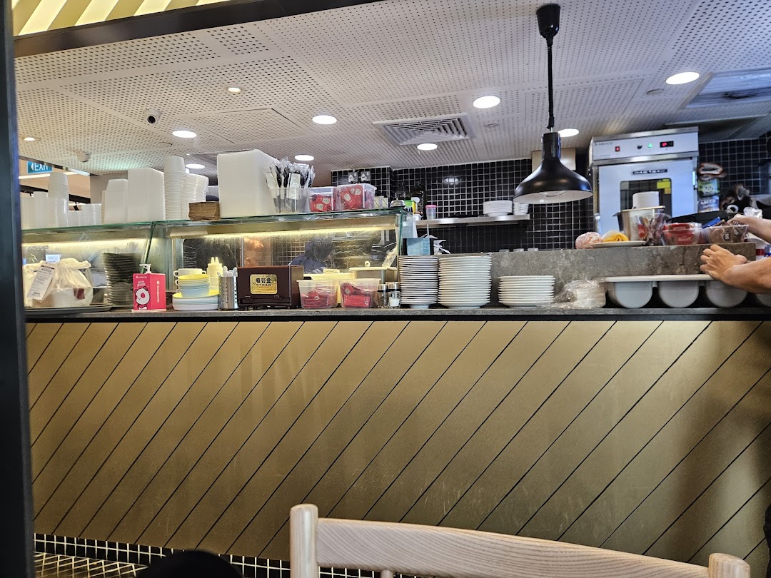 A bustling restaurant counter with stacked dishes, cups, and kitchen equipment in the background.