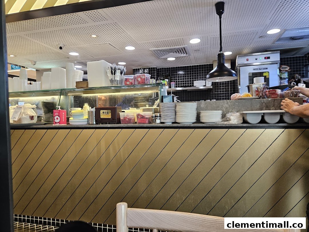 A bustling restaurant counter with stacked dishes, cups, and kitchen equipment in the background.
