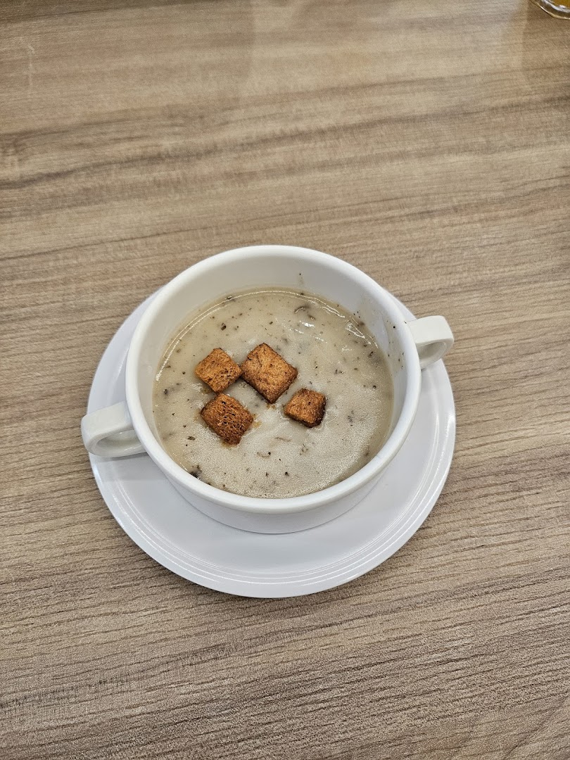 A warm bowl of creamy mushroom soup topped with golden croutons on a wooden table.