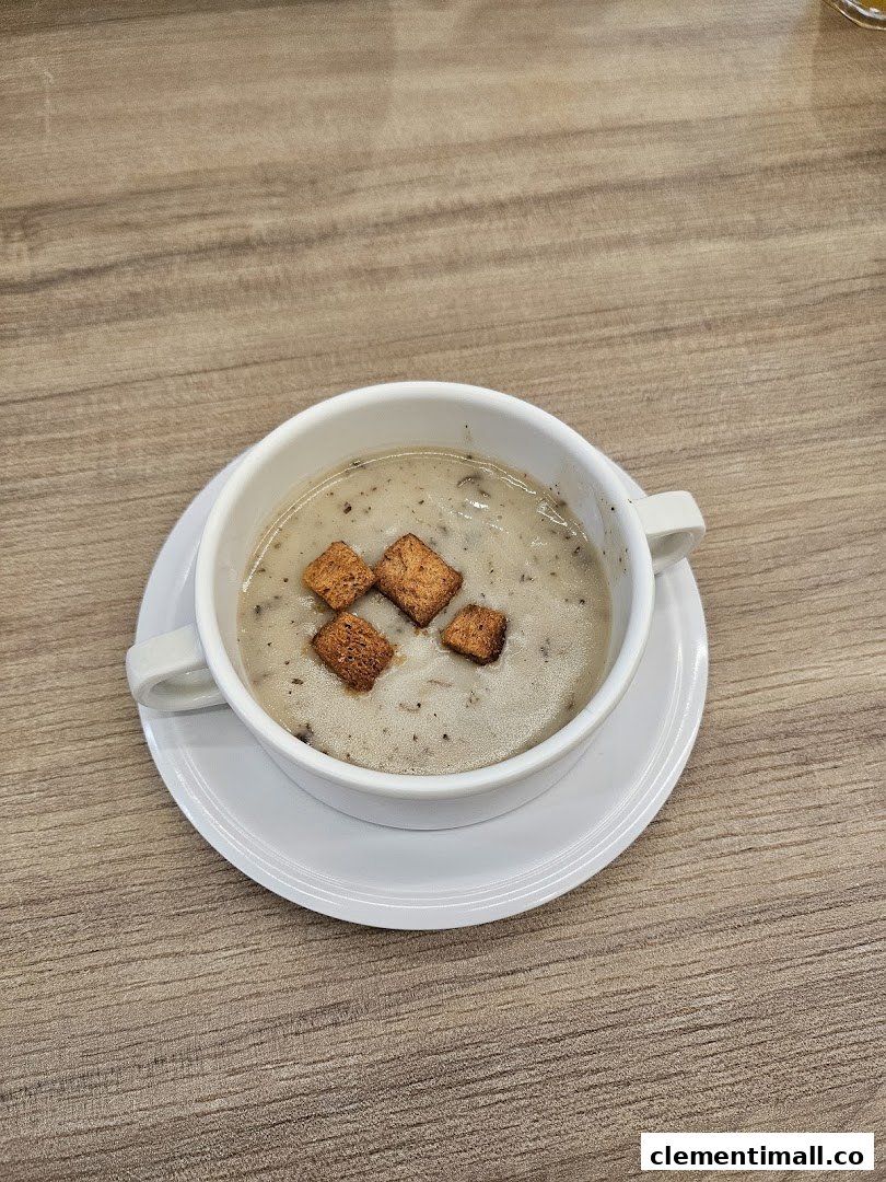 A warm bowl of creamy mushroom soup topped with golden croutons on a wooden table.