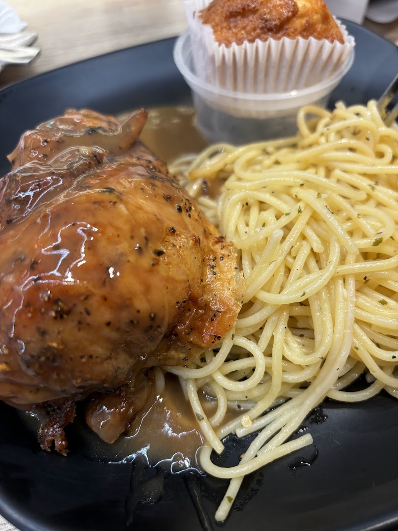 A close-up of roasted chicken with gravy, spaghetti, and a muffin on a black plate.