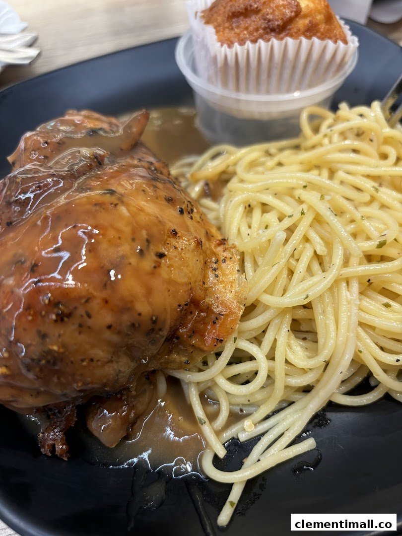 A close-up of roasted chicken with gravy, spaghetti, and a muffin on a black plate.