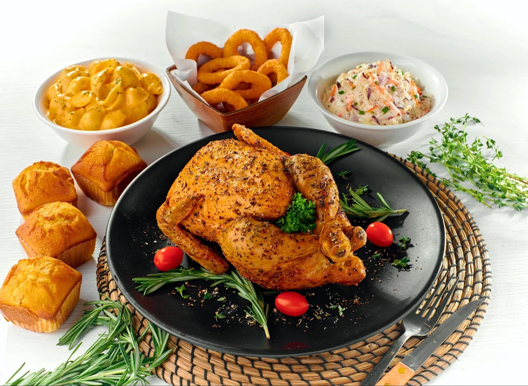 A perfectly roasted chicken with mac and cheese, onion rings, coleslaw, and corn muffins.