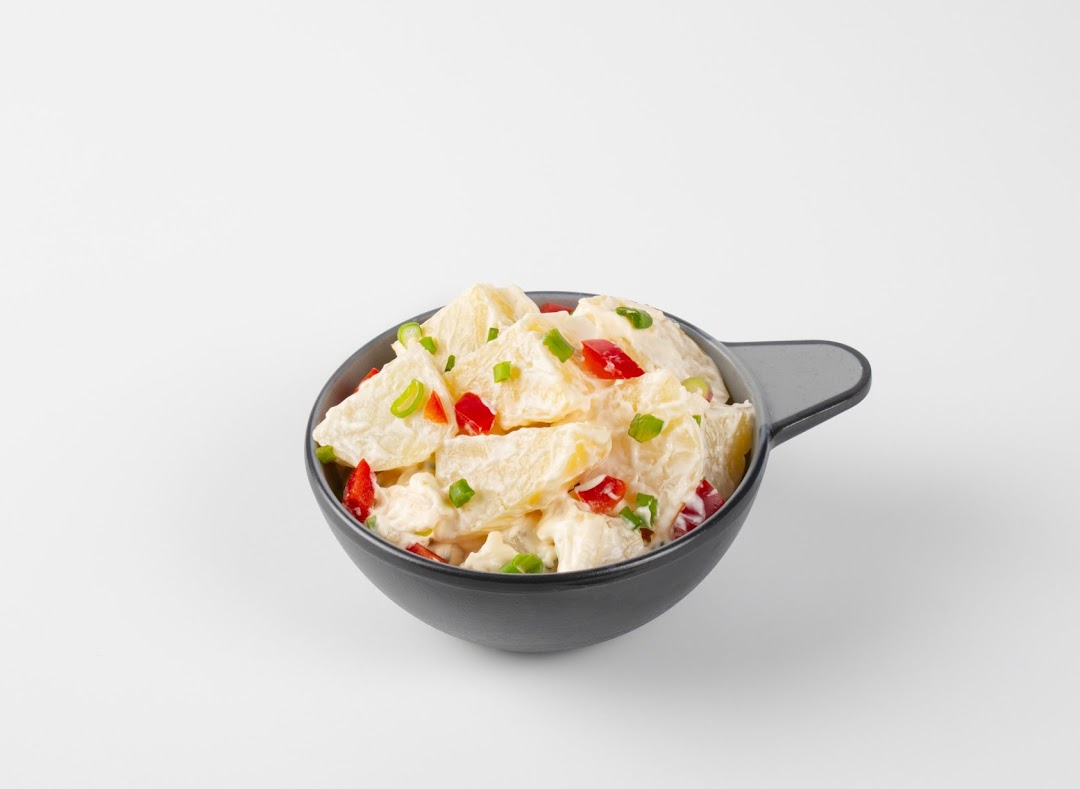 A bowl of creamy potato salad with diced red bell peppers and green onions.