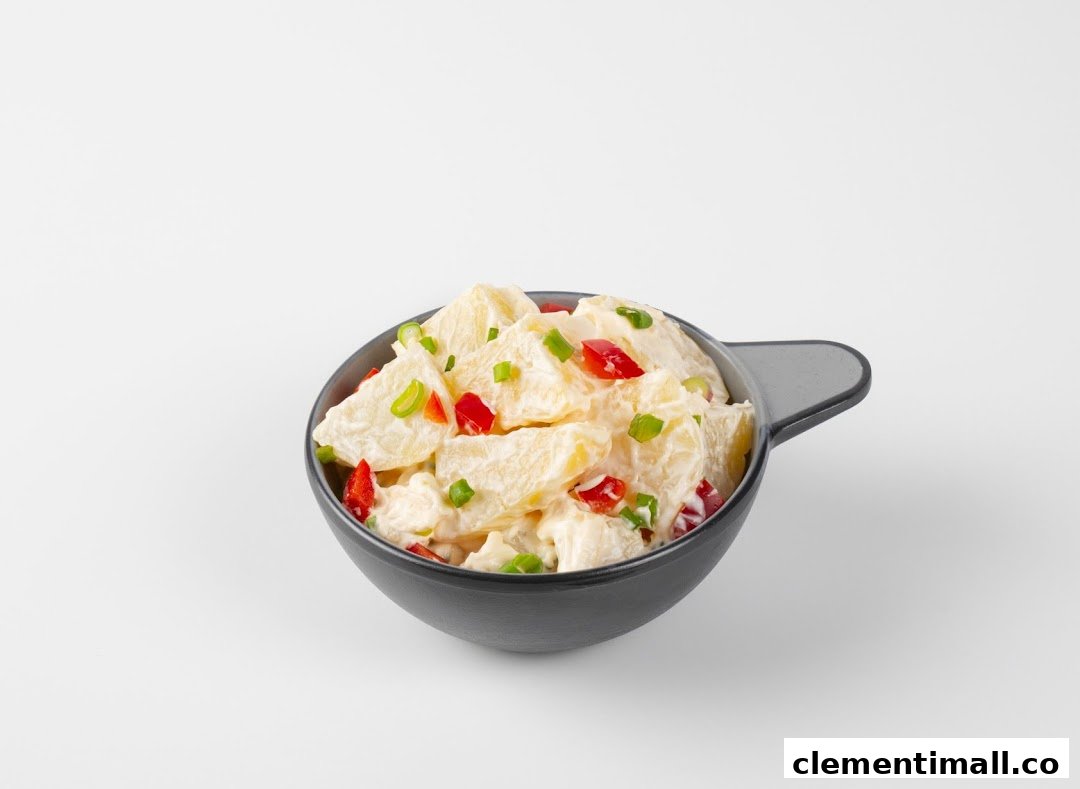 A bowl of creamy potato salad with diced red bell peppers and green onions.