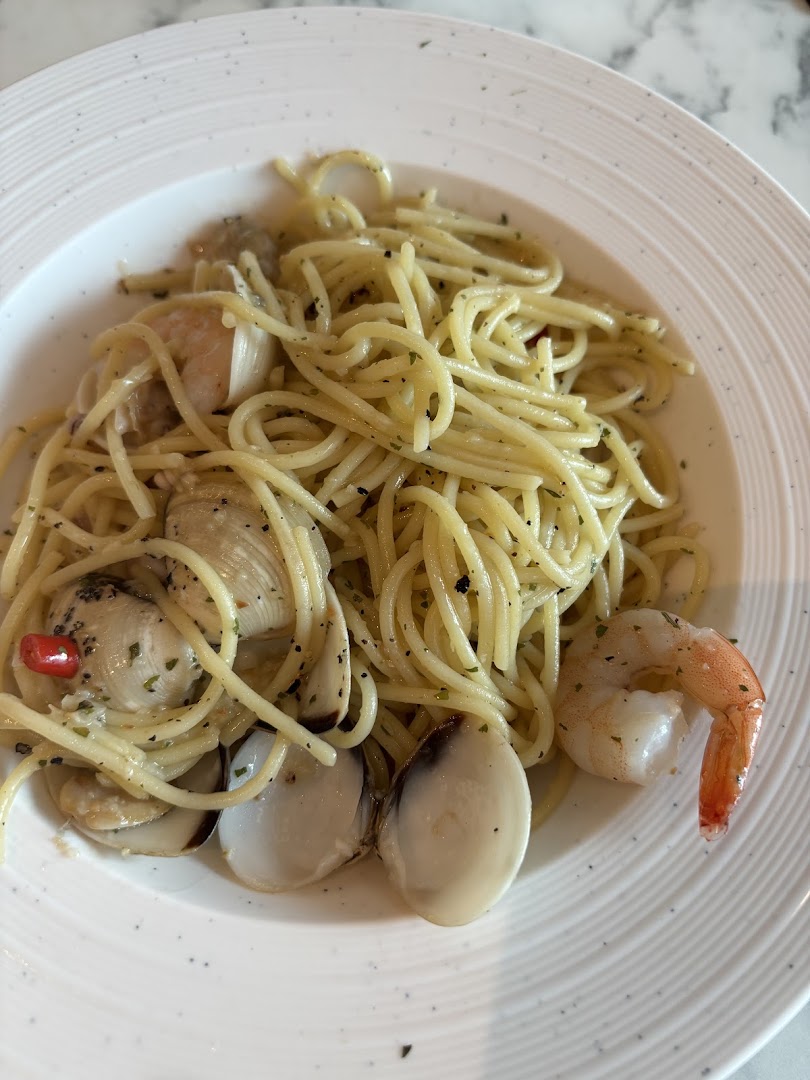 A close-up of a plate of spaghetti with clams, shrimp, and herbs.