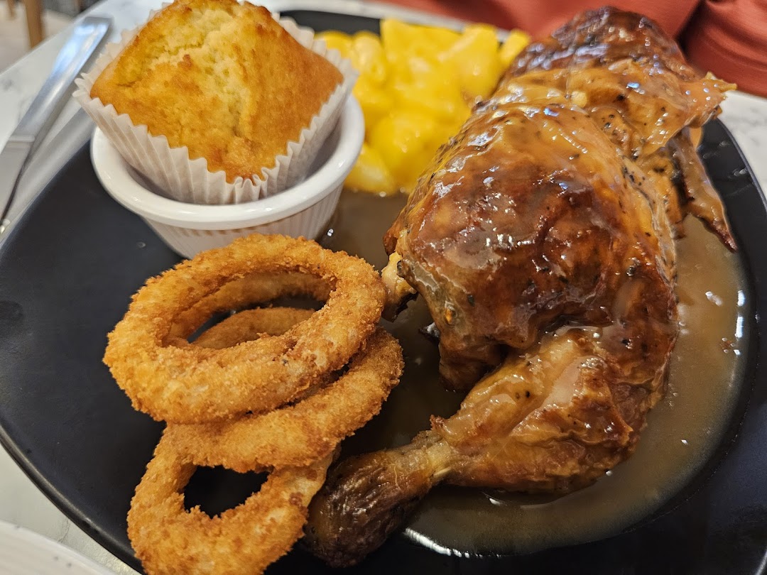 A delicious plate featuring roasted chicken, crispy onion rings, a golden muffin, and a creamy side dish.