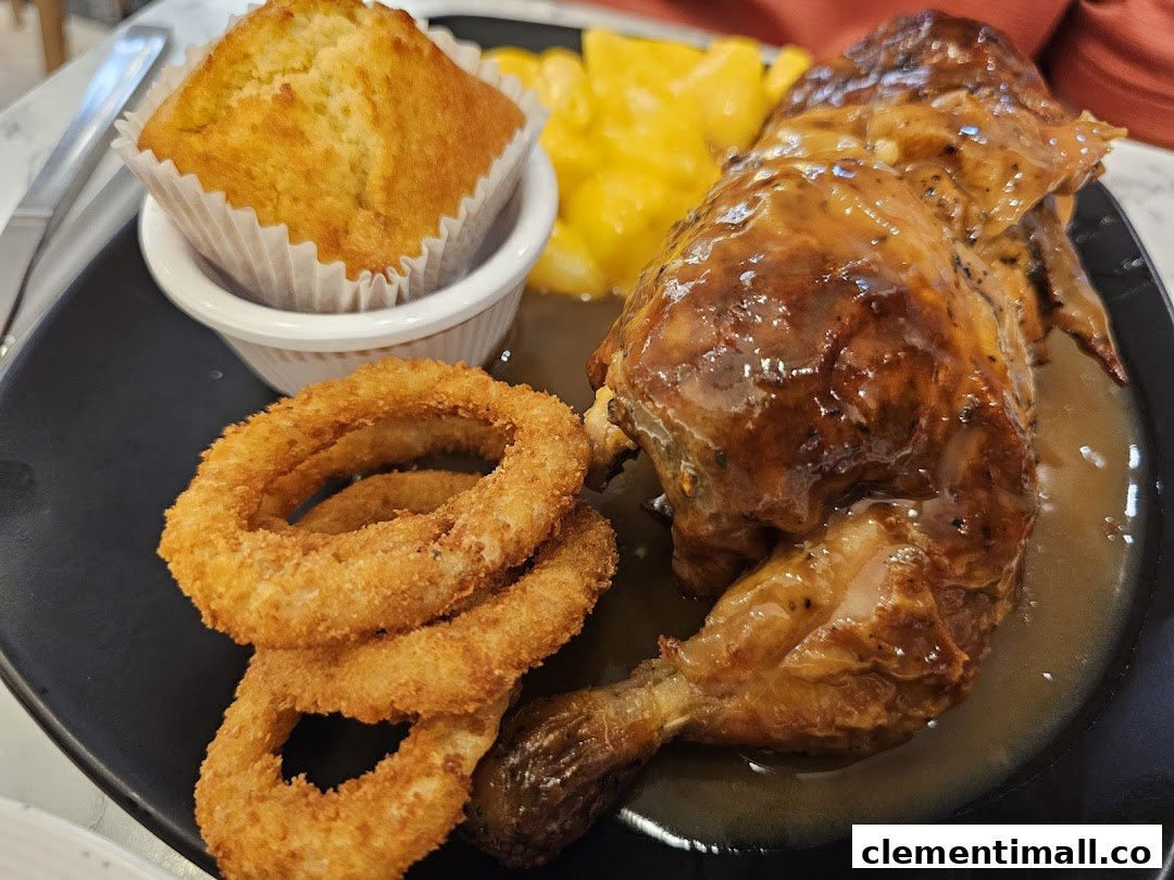 A delicious plate featuring roasted chicken, crispy onion rings, a golden muffin, and a creamy side dish.