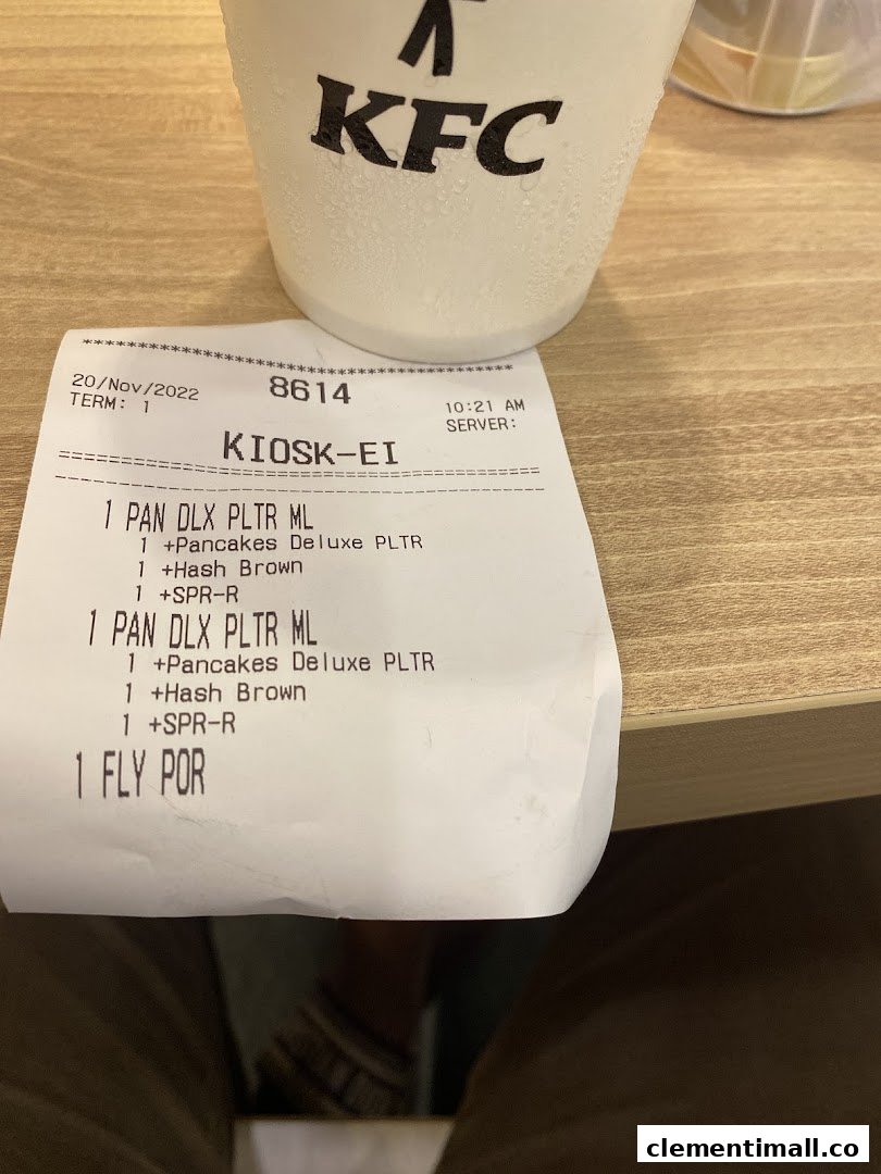 A KFC receipt showing breakfast items and a condensation-covered KFC cup on a wooden table.