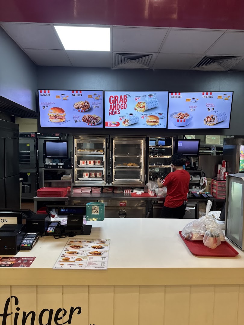 Interior view of KFC Clementi Mall featuring digital menu boards and a staff member at the counter.