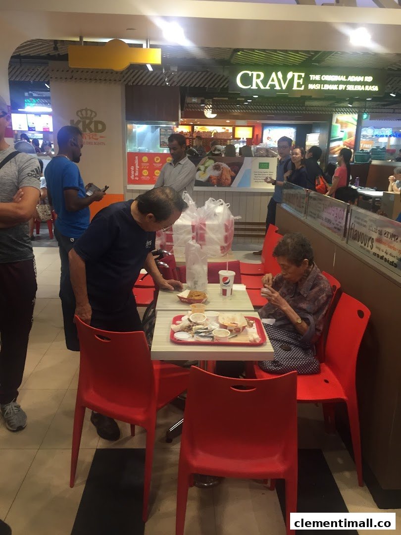 Customers enjoy meals at tables with red chairs in a bustling food court, with other eateries visible.