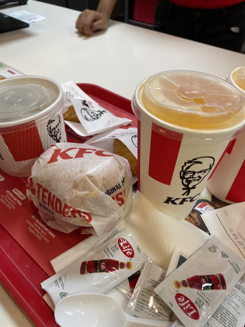 A tray of KFC food, including a burger, drinks, and sauces, on a white table.