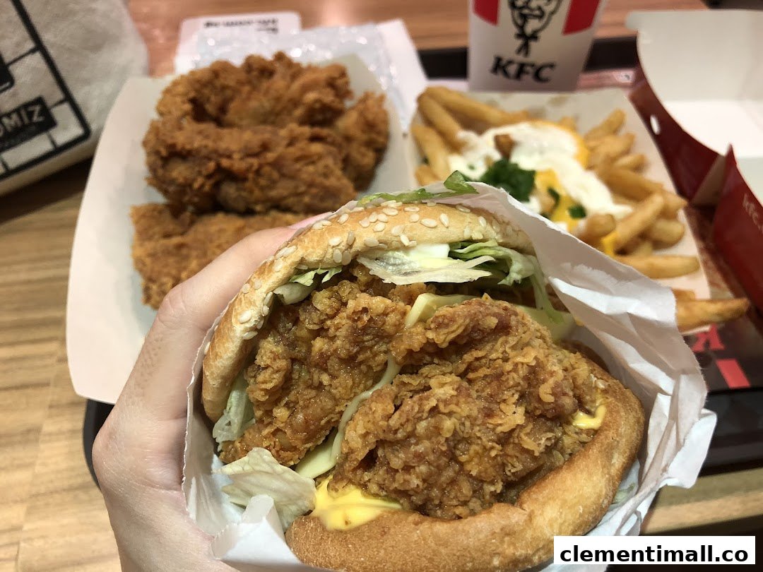 A hand holding a crispy KFC Zinger burger with fried chicken and loaded fries in the background.