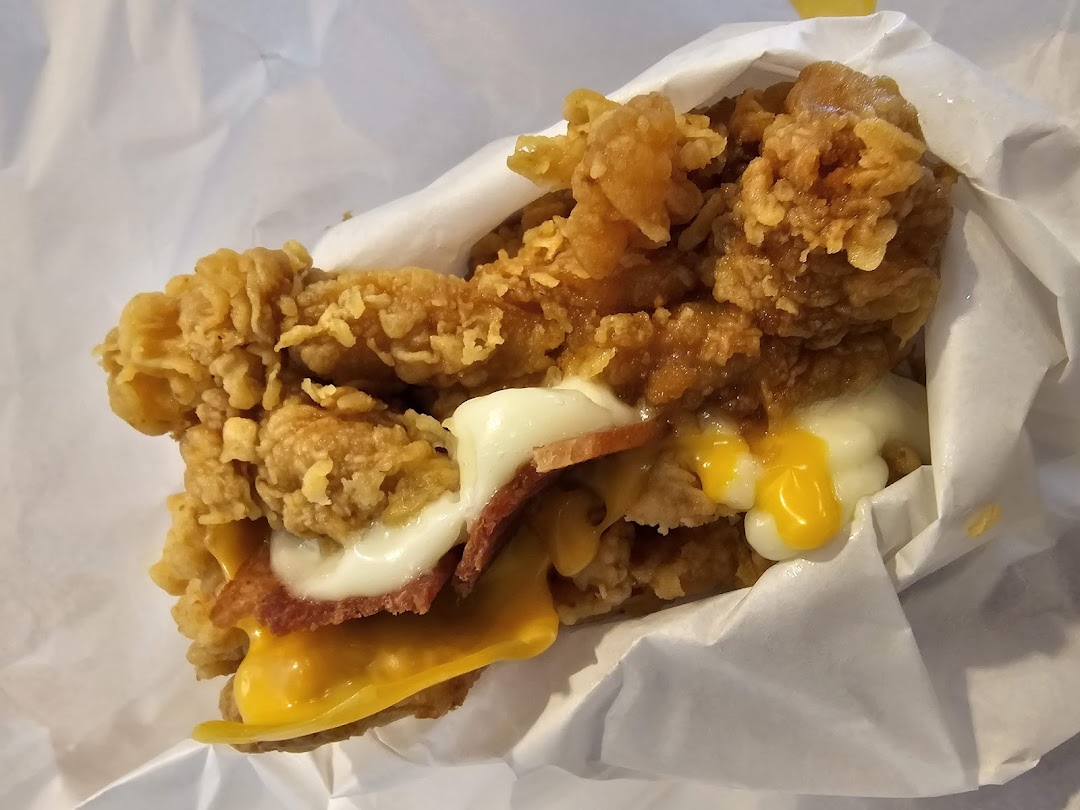 A close-up of a delicious fried chicken sandwich with cheese, bacon, and sauce, wrapped in paper.