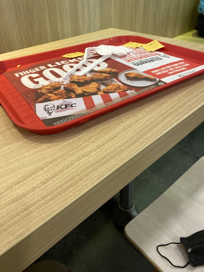A red KFC tray with a promotional liner featuring fried chicken and the KFC logo on a wooden table.