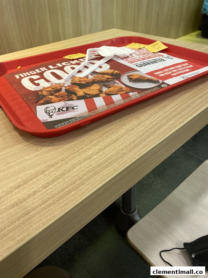 A red KFC tray with a promotional liner featuring fried chicken and the KFC logo on a wooden table.