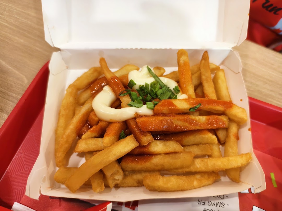 A close-up of KFC's golden fries topped with spicy sauce, creamy mayonnaise, and fresh spring onions.
