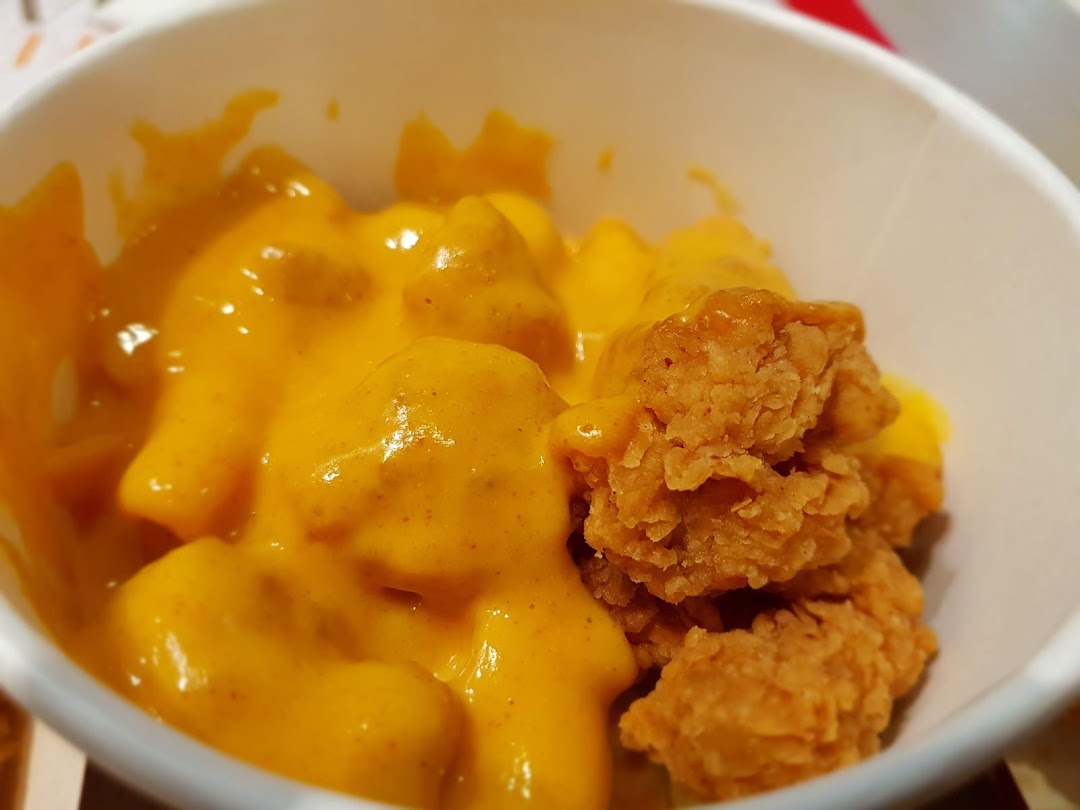 Close-up of KFC's golden fried chicken bites with creamy, rich cheese sauce in a cup.