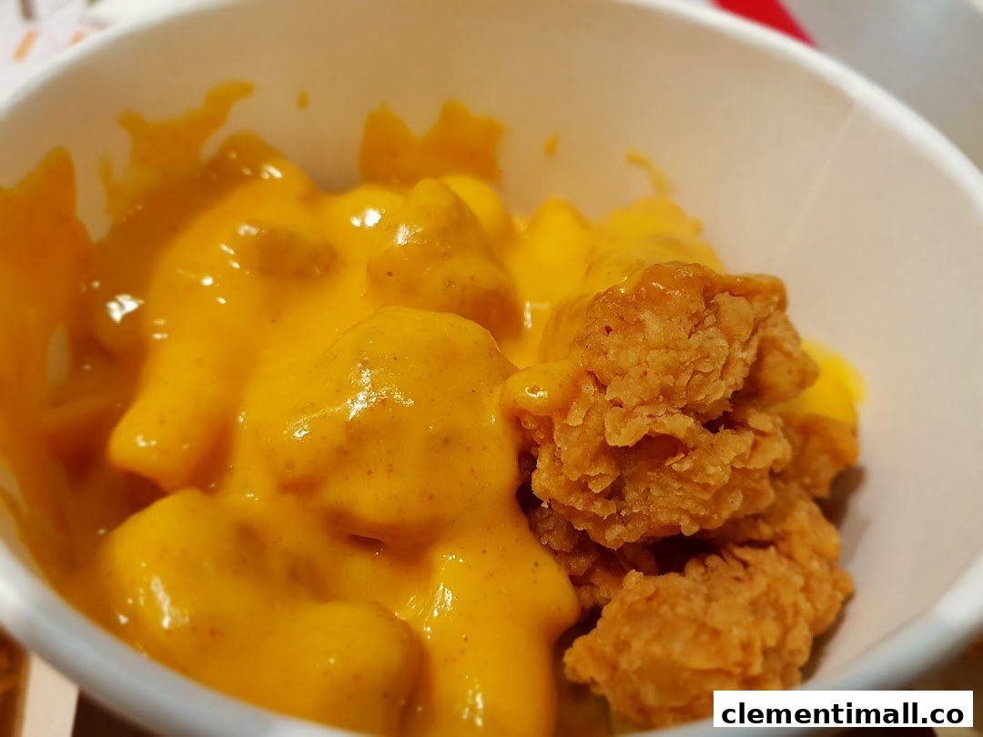 Close-up of KFC's golden fried chicken bites with creamy, rich cheese sauce in a cup.