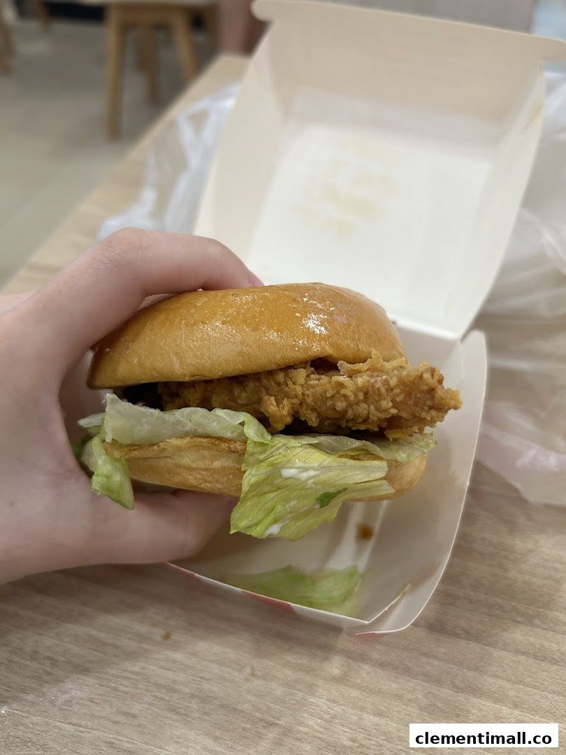 A hand holds a golden crispy chicken burger with fresh lettuce and sauce, presented in its box.