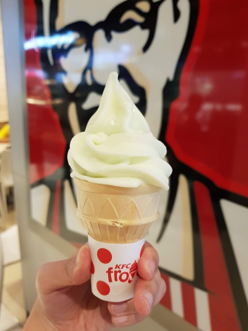 A hand holds a refreshing KFC froyo soft-serve ice cream cone inside the restaurant.