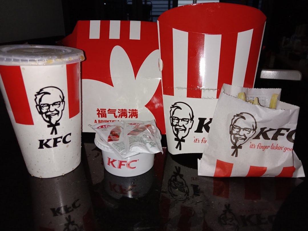 A close-up of various KFC food items, including a drink, fries, and chicken packaging.