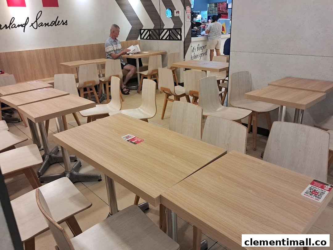 The image shows the clean and modern dining area of KFC, with light wood tables and chairs, and a customer seated.