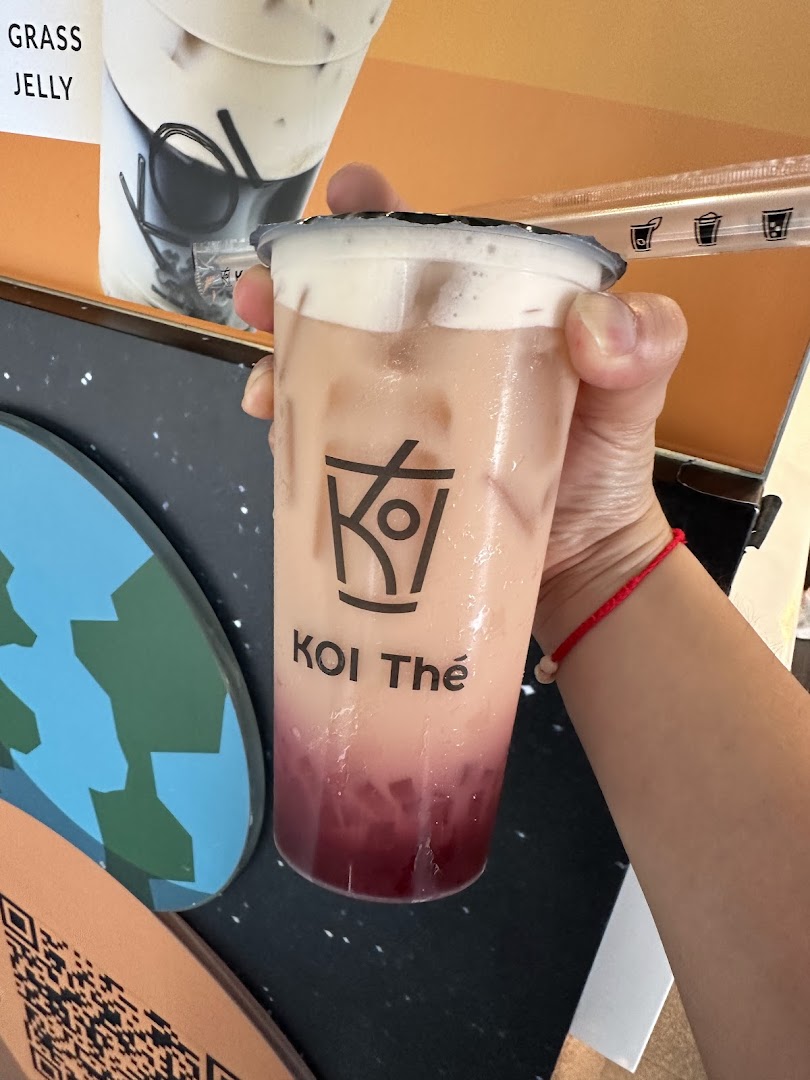 A hand holds a refreshing KOI Thé bubble tea with a creamy top layer and red jelly.