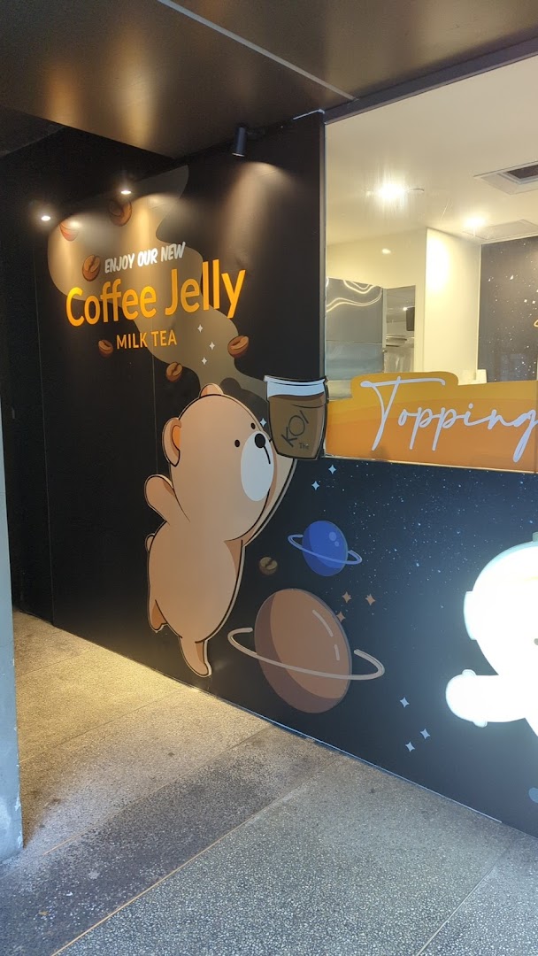 A promotional wall at KOI Thé featuring a cartoon bear and 'Coffee Jelly Milk Tea' advertisement.