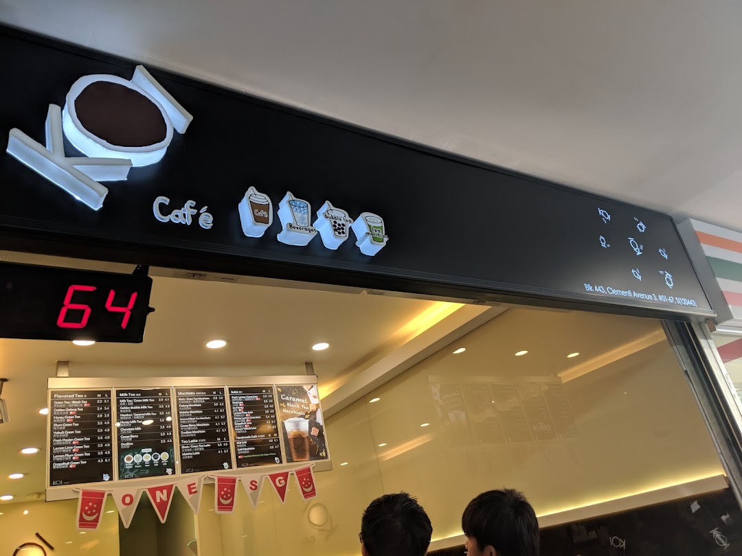 The illuminated KOI Thé shopfront with its distinctive logo, queue number display, and visible menu board.