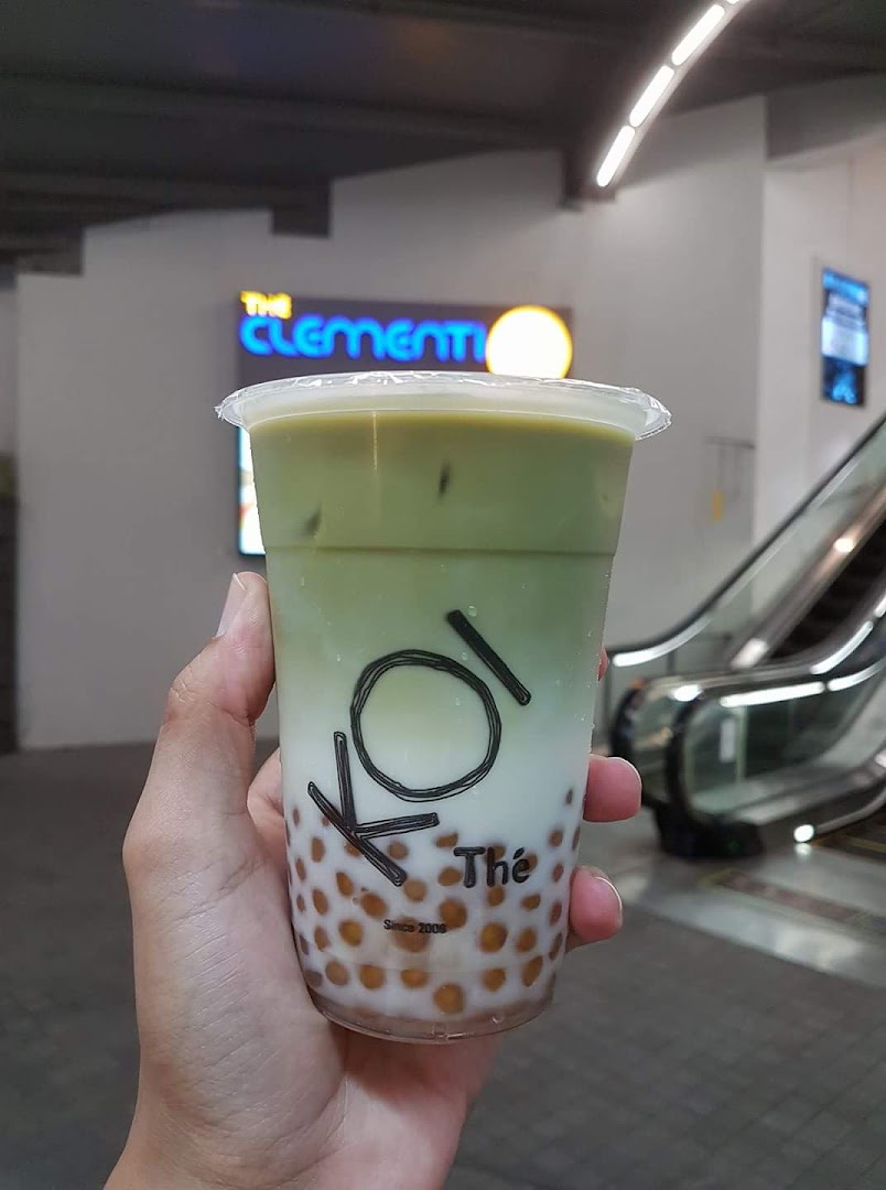 A hand holds a KOI Thé bubble tea drink with 'The Clementi' mall sign in the background.