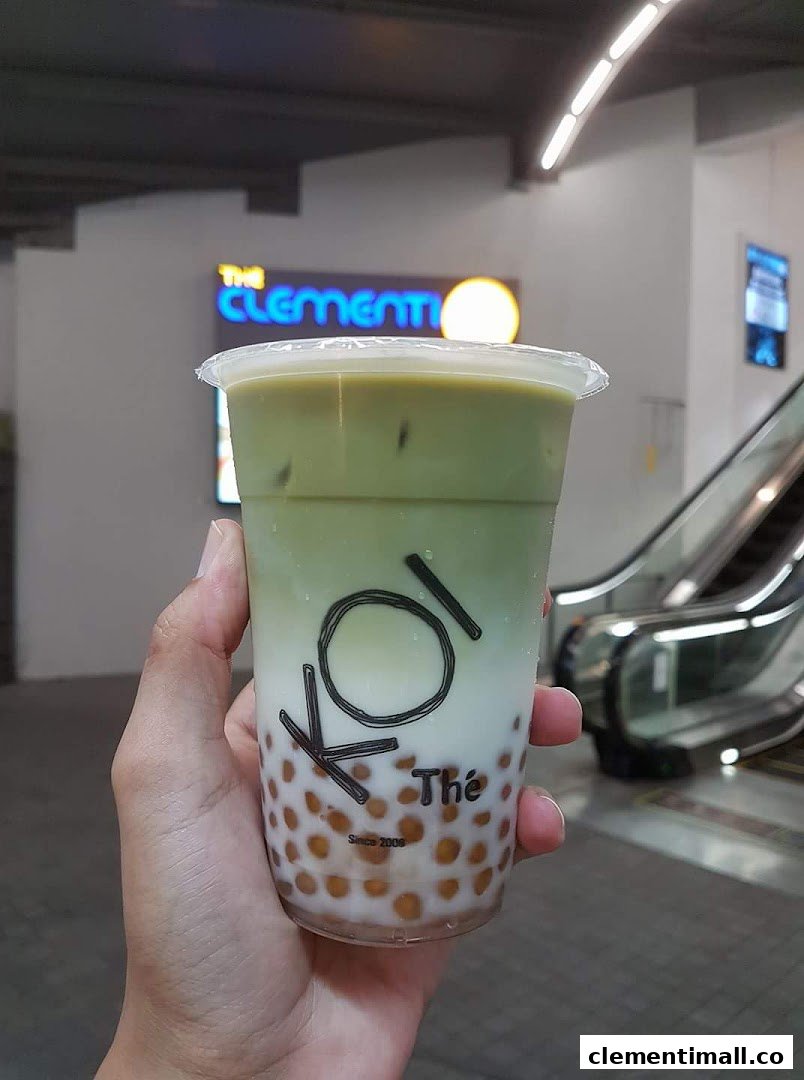 A hand holds a KOI Thé bubble tea drink with 'The Clementi' mall sign in the background.