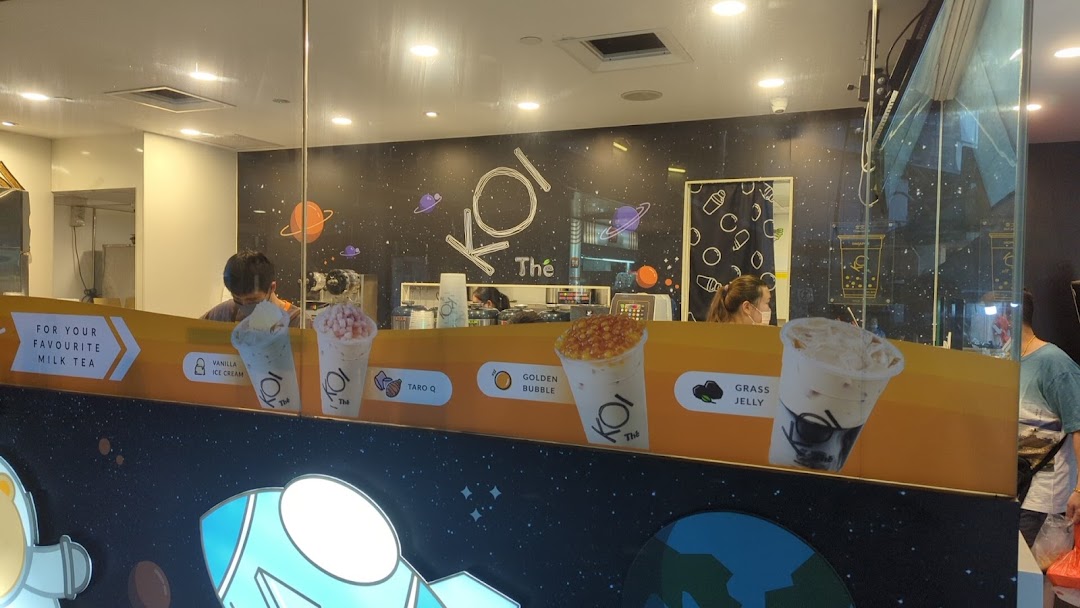 The shop front of KOI Thé, featuring staff, a space-themed interior, and promotional images of popular bubble tea drinks.