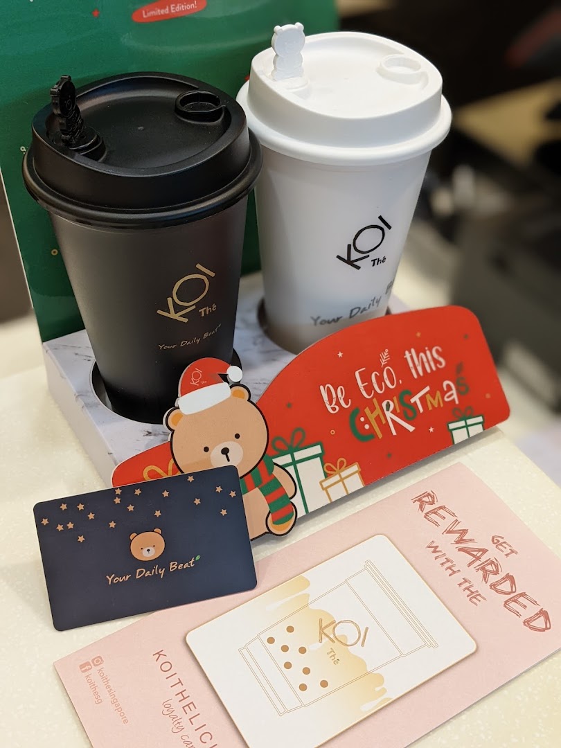 Two KOI Thé reusable cups, loyalty cards, and a festive 'Be Eco this Christmas' card.