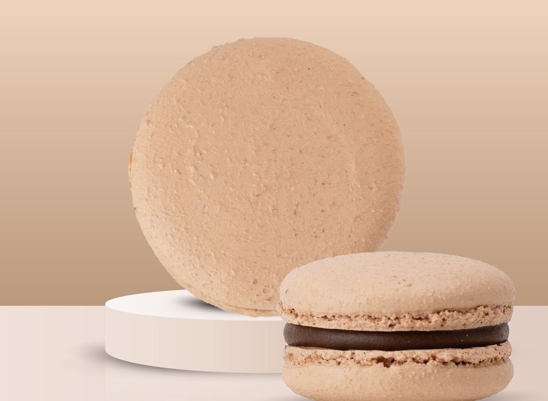 Two light brown macarons, one whole and one with a chocolate filling, on a minimalist background.