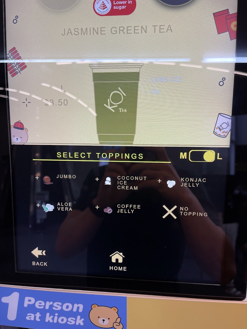 A digital kiosk screen at KOI Thé displaying Jasmine Green Tea options and various toppings for customization.