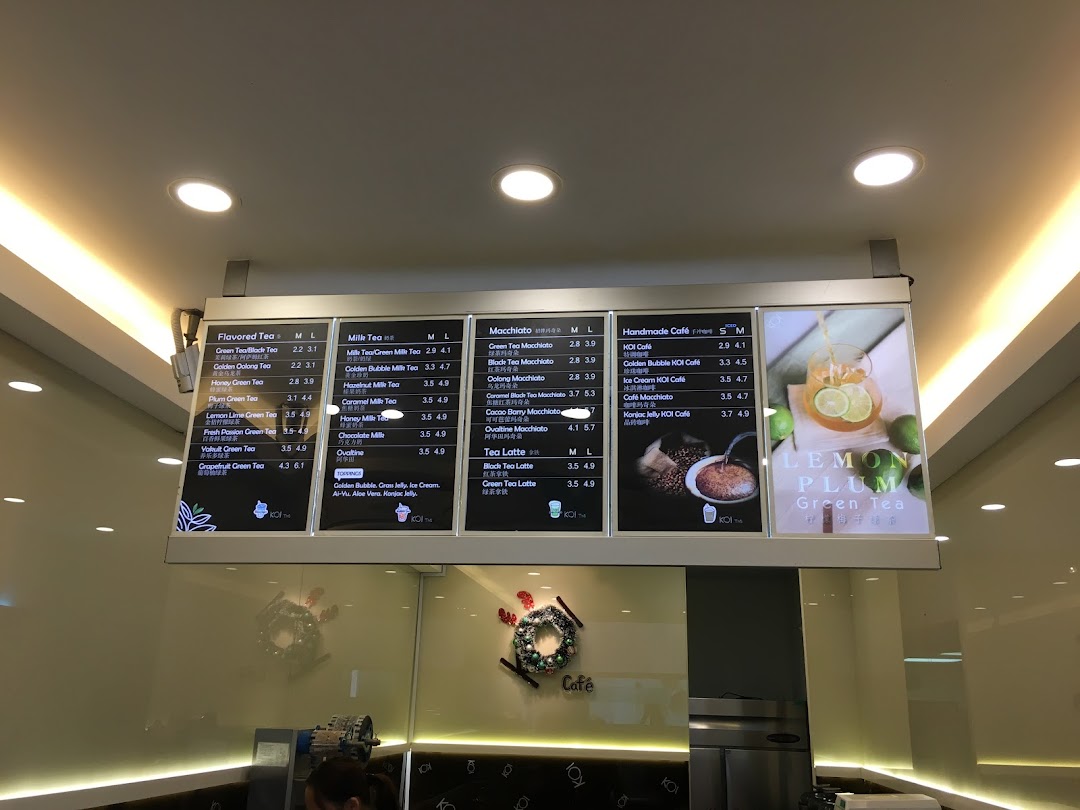 A bright menu board displaying various tea and coffee beverages with prices at KOI Thé.