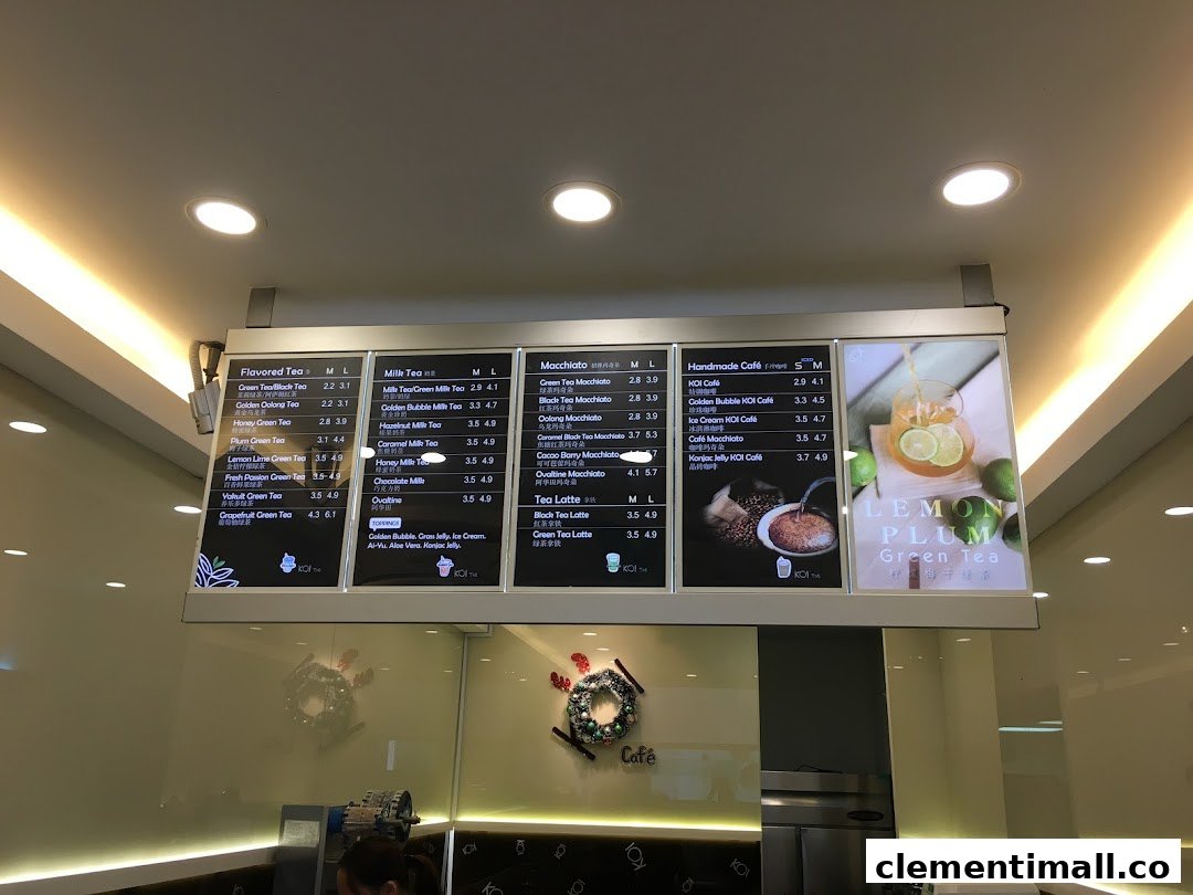 A bright menu board displaying various tea and coffee beverages with prices at KOI Thé.