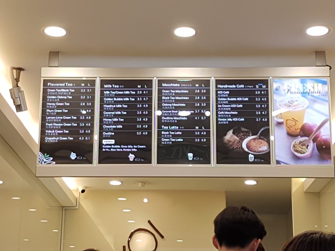 A brightly lit menu board displaying various bubble tea and coffee options at KOI Thé.