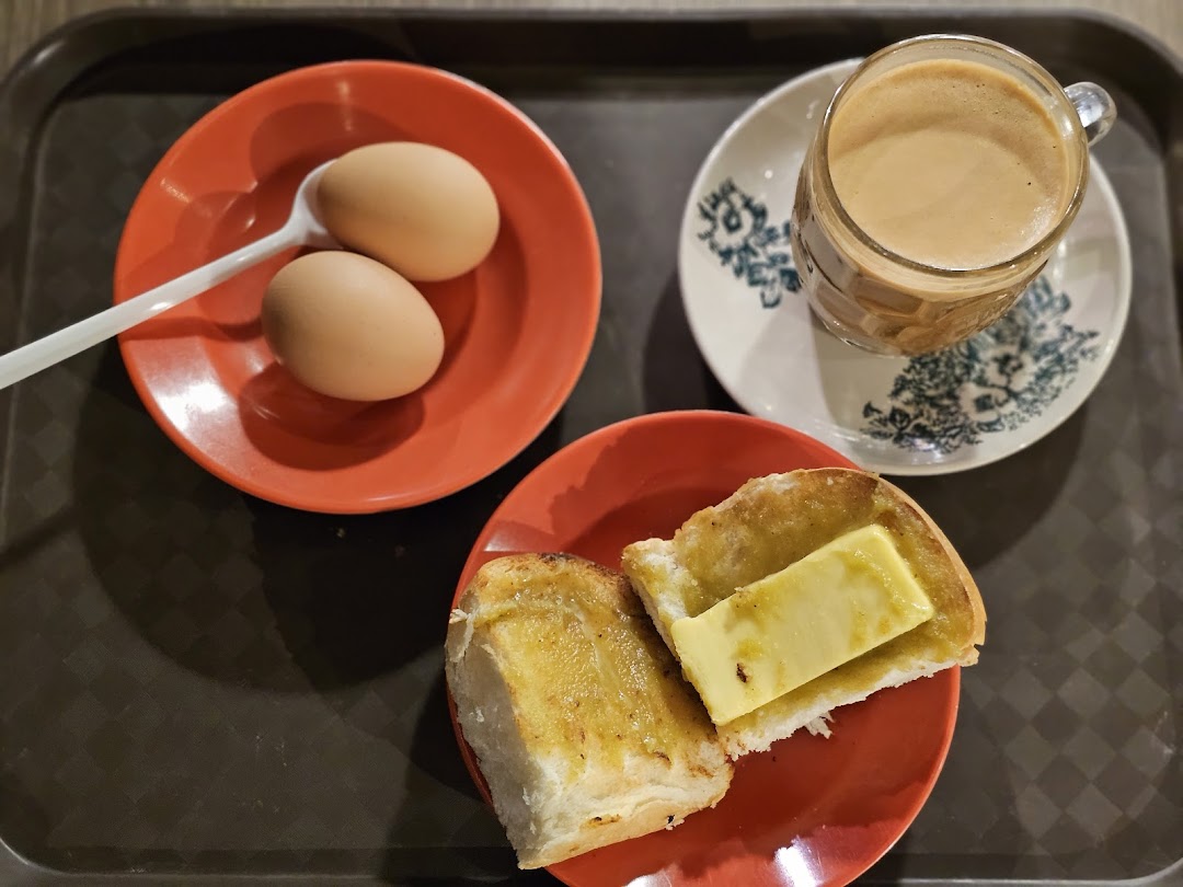 A classic breakfast set featuring soft-boiled eggs, kaya toast with butter, and a cup of coffee.
